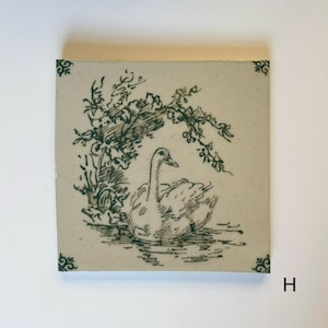 Può includere: Piastrella quadrata in ceramica con un'illustrazione disegnata a mano di un cigno sull'acqua, sotto il fogliame. L'opera d'arte è in verde scuro su sfondo crema. Accenti decorativi agli angoli e la lettera "H" visibili.