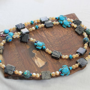May include: A multi-strand necklace with a silver clasp. The necklace features square black and white stones, small round beige stones, and turquoise turtle charms.
