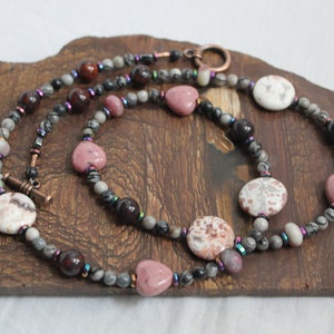 May include: A multi-strand necklace with pink heart-shaped beads, round white and gray beads, and dark red beads. The necklace is made with copper wire and has a copper clasp.