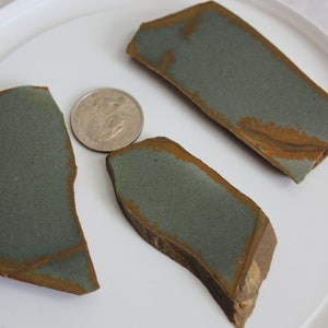 May include: Three pieces of green and brown agate, each with a unique shape and pattern. The agate is a semi-precious stone that is often used in jewelry and other decorative items.