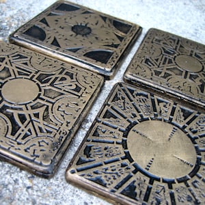 May include: Four gold-colored metal puzzle boxes with intricate designs. Each box has a different pattern and a circular center piece.