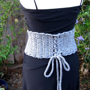 May include: A gray crocheted corset with a lace-up back. The corset is tied at the front with long gray strings.