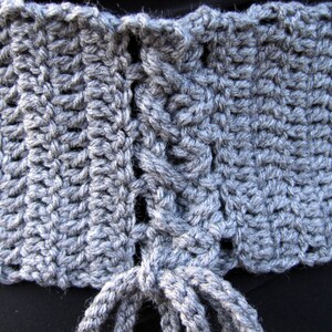 May include: A gray crocheted belt with a lace-up back. The belt is made of a soft, textured yarn and has a simple, elegant design.