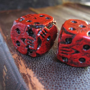 May include: Two red dice with a textured surface and black markings. The dice are sitting on a brown leather surface.