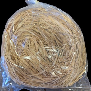 May include: A clear plastic bag filled with a large amount of natural, light brown, shredded paper. The paper is tightly packed and appears to be made from natural fibers.