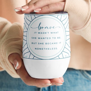 May include: White insulated wine tumbler with a teal and white geometric design. The tumbler features the word "brave" in cursive, along with the quote: "IT WASN'T WHAT SHE WANTED TO BE. BUT SHE BECAME IT NONETHELESS."