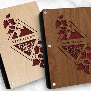 May include: Two wooden wine tasting journals with black edging. The covers feature a red diamond with a vine design and the text "tasting notes". One journal has the name "Jennifer's" above the diamond and the other has the word "Wine" above the diamond.