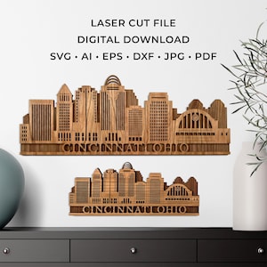 Puede incluir: Dos piezas de arte mural de madera cortadas con láser que representan el horizonte de Cincinnati, Ohio. El texto "CINCINNATI OHIO" está tallado en la base de cada pieza. La parte superior de la imagen tiene el texto "LASER CUT FILE DIGITAL DOWNLOAD" y opciones de tipo de archivo.