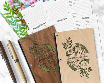 May include: Two wooden garden journals with laser-cut floral designs and personalized text reading David's Garden and Isabella's Garden. Includes two wooden pens and several printed planner pages with sections for notes, shopping, and plant logs.