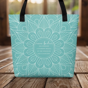 May include: A teal blue tote bag with a white mandala design and the text "never broken she emerged a stunning mosaic of the struggles she'd overcome".