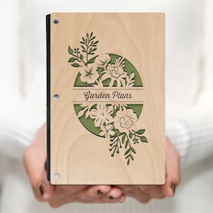 Op de afbeelding: Een houten dagboek met een groen bloemmotief en de tekst "Garden Plans" op de voorkant.