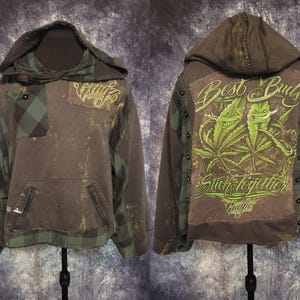 May include: A charcoal grey and green plaid hooded sweatshirt featuring a front kangaroo pocket and a distressed finish. The back displays a large green graphic of two anthropomorphic leaves with the text Best Buds Stick Together.