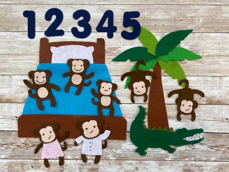 May include: Felt board set with five brown monkeys, a green alligator, a brown palm tree, and a brown bed with a blue blanket. The numbers 1, 2, 3, 4, and 5 are displayed at the top of the board.