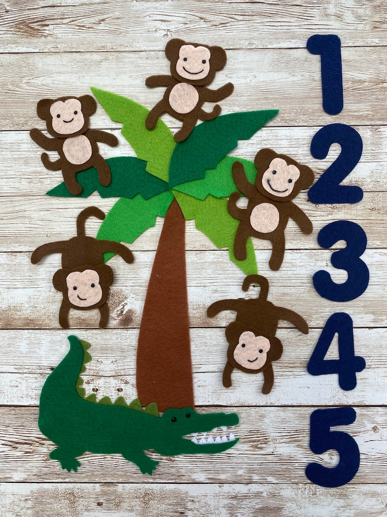 May include: A felt play set with five brown monkeys, a green alligator, and a brown palm tree. The monkeys are climbing the palm tree and the alligator is at the bottom of the tree. There are blue felt numbers 1 through 5 on the right side of the image.
