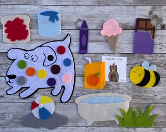 May include: A collection of felt shapes including a white dog with colorful spots, a piece of toast with red jam, a blue paint bucket, a purple crayon, a pink ice cream cone, a chocolate bar, a juice box, a bee, a ball, a tub, and grass.
