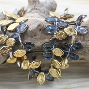 May include: A strand of glass beads in shades of blue and gray, with gold leaf accents. The beads are shaped like leaves and are strung together on a clear thread.