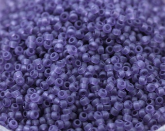 May include: A close-up view of a large quantity of small, round, opaque purple beads. The beads are arranged in a random pattern, creating a textured surface.