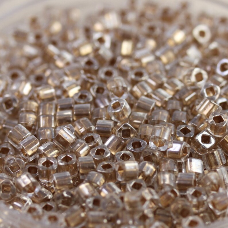 May include: A close-up view of a large quantity of small, clear glass beads with a gold iridescent sheen.