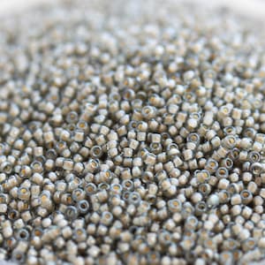 以下が含まれることがあります： 小さな丸いガラスビーズがたくさんあるクローズアップ。ビーズは薄いベージュ色で、わずかに光沢があります。ランダムなパターンで配置されており、質感のある表面になっています。