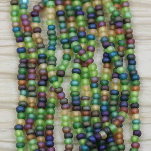 May include: A strand of iridescent glass beads in shades of green, blue, brown, and yellow. The beads are small and round, and they have a matte finish.