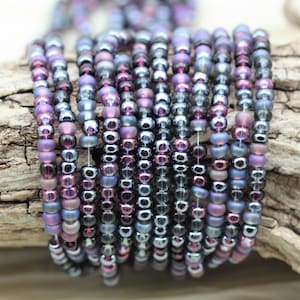May include: A strand of iridescent purple and silver seed beads. The beads are small and round, and they have a metallic sheen.