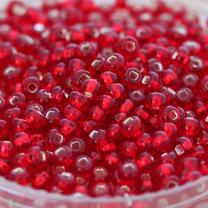 May include: A close-up image of a large quantity of small, round, red glass beads. The beads are translucent and have a slight shimmer.