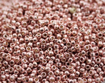May include: A close-up shot of a pile of small, metallic rose gold beads. The beads are round with a hole through the center, and they reflect light, creating a shiny appearance. The beads are scattered, filling the frame.