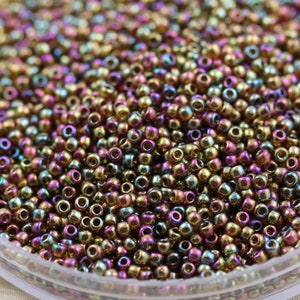 May include: A close-up view of a large quantity of small, round, iridescent beads in shades of gold, purple, and green. The beads are arranged in a random pattern and appear to be made of glass.