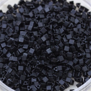 May include: A close-up image of a pile of small, black, square-shaped beads with a triangular hole in the center.