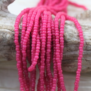 May include: A strand of pink glass seed beads. The beads are small and round, and they are strung on a thin thread. The beads are a bright, vibrant pink color.