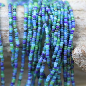 May include: A strand of small, round glass beads in shades of blue, green, and purple. The beads are arranged in a random pattern, creating a colourful and eye-catching display.