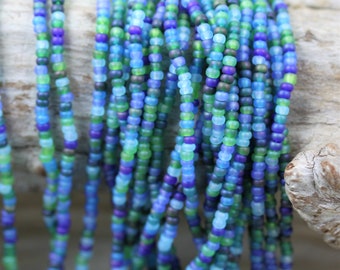 May include: A strand of small, round glass beads in shades of blue, green, and purple. The beads are arranged in a random pattern, creating a colorful and eye-catching display.