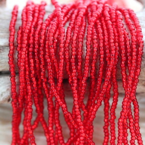 Puede incluir: Primer plano de un paquete de cuentas de semillas rojas. Las cuentas son pequeñas y redondas, y están dispuestas en un patrón suelto y fluido.