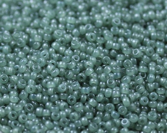 May include: A close-up view of a large quantity of small, round, opaque green beads. The beads are arranged in a random pattern and appear to be made of glass or plastic.