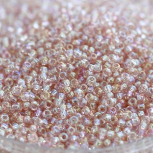 May include: A close-up of a large quantity of small, iridescent pink seed beads. The beads are translucent and have a slight shimmer.