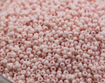 May include: A close-up view of a large quantity of small, round, light pink beads. The beads are arranged in a random pattern and are all the same size.