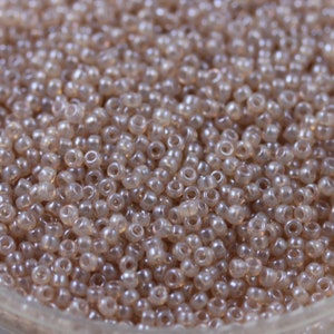 Puede incluir: Vista de cerca de una gran cantidad de pequeñas cuentas redondas translúcidas de color marrón claro. Las cuentas tienen un ligero brillo iridiscente.