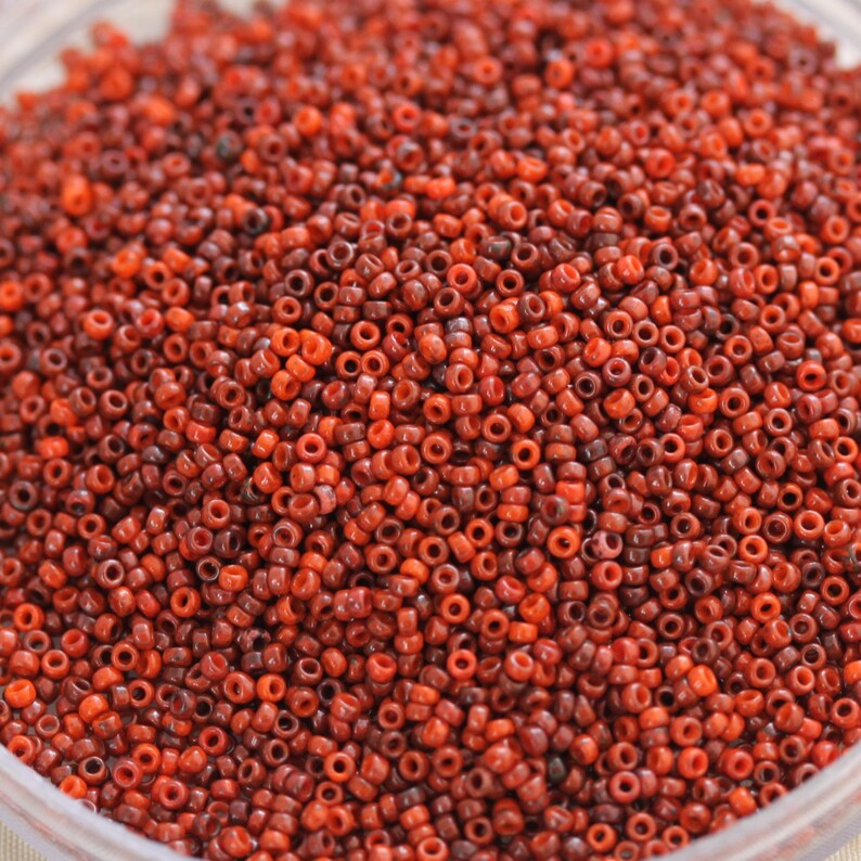 May include: A close-up image of a large quantity of small, round, red and brown beads. The beads are all the same size and shape, and they are arranged in a random pattern.