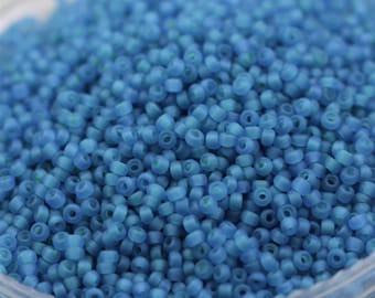 May include: A close-up view of a container filled with small, opaque, light blue seed beads. The beads are round and have a slightly frosted finish.
