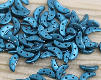 May include: A pile of teal blue crescent-shaped beads with three holes each. The beads are made of glass and have a metallic finish.