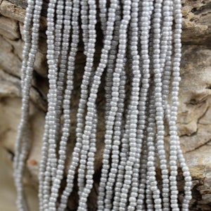 Könnte beinhalten: Nahaufnahme einer Schnur grauer Perlen. Die Perlen sind klein und rund und auf einem dünnen Faden aufgereiht. Die Perlen sind vertikal angeordnet und erzeugen eine glatte, gleichmäßige Textur.