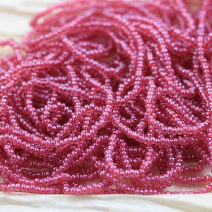 May include: A close-up of a pile of pink seed beads. The beads are small and round, and they have a slight sheen to them.