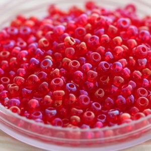 May include: A close-up of a bowl filled with small, red, iridescent glass beads. The beads are round and have a shiny, reflective surface.