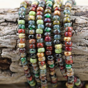 May include: A strand of colorful glass beads with a variety of patterns and textures. The beads are small and round, and they are strung together on a clear thread. The beads are a mix of red, green, brown, and yellow.