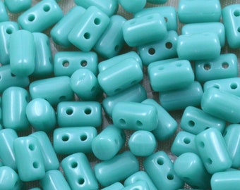 May include: A close-up of a pile of turquoise blue glass beads. The beads are rectangular in shape with two holes in each bead.