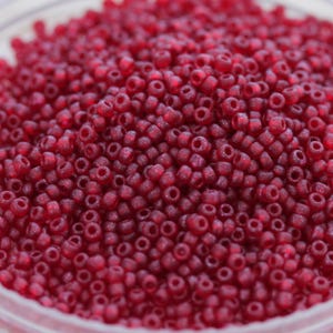 Può includere: Una vista ravvicinata di una grande quantità di piccole perline rotonde di colore rosso. Le perline hanno una finitura leggermente iridescente, che conferisce loro un leggero bagliore.