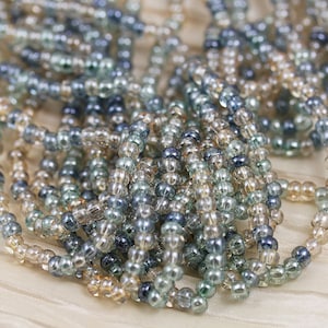 May include: A close-up of a pile of small, round, glass beads in shades of blue and beige. The beads are translucent and have a slight iridescent sheen.