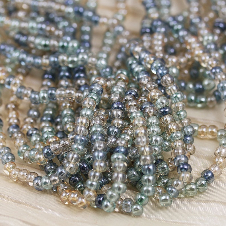 May include: A close-up of a pile of small, round, glass beads in shades of blue and beige. The beads are translucent and have a slight iridescent sheen.