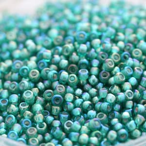 Op de afbeelding: Een close-up van een grote hoeveelheid kleine, ronde, turquoise glazen kralen. De kralen hebben een licht iriserende afwerking.