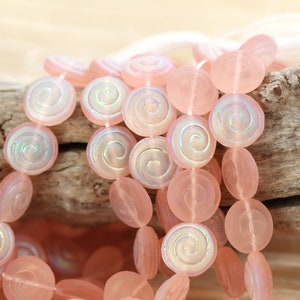 Op de afbeelding: Een streng roze glazen kralen met een swirl-ontwerp. De kralen zijn doorschijnend en hebben een iriserende afwerking.